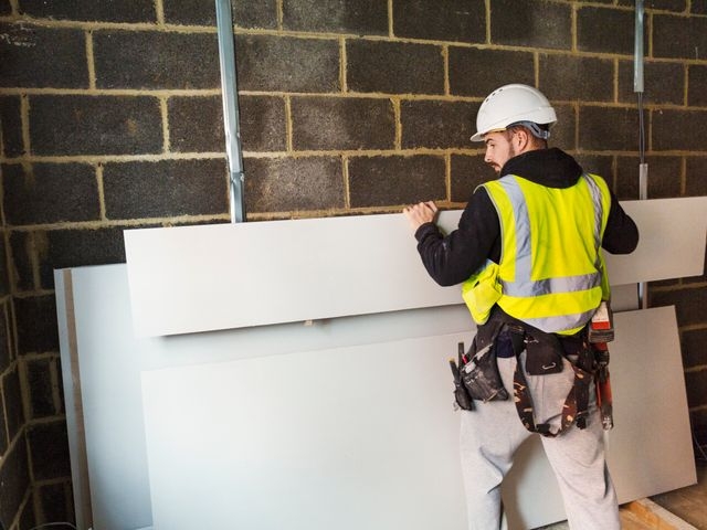 A workman in hard hat and high vis jacket stacking plasterboard